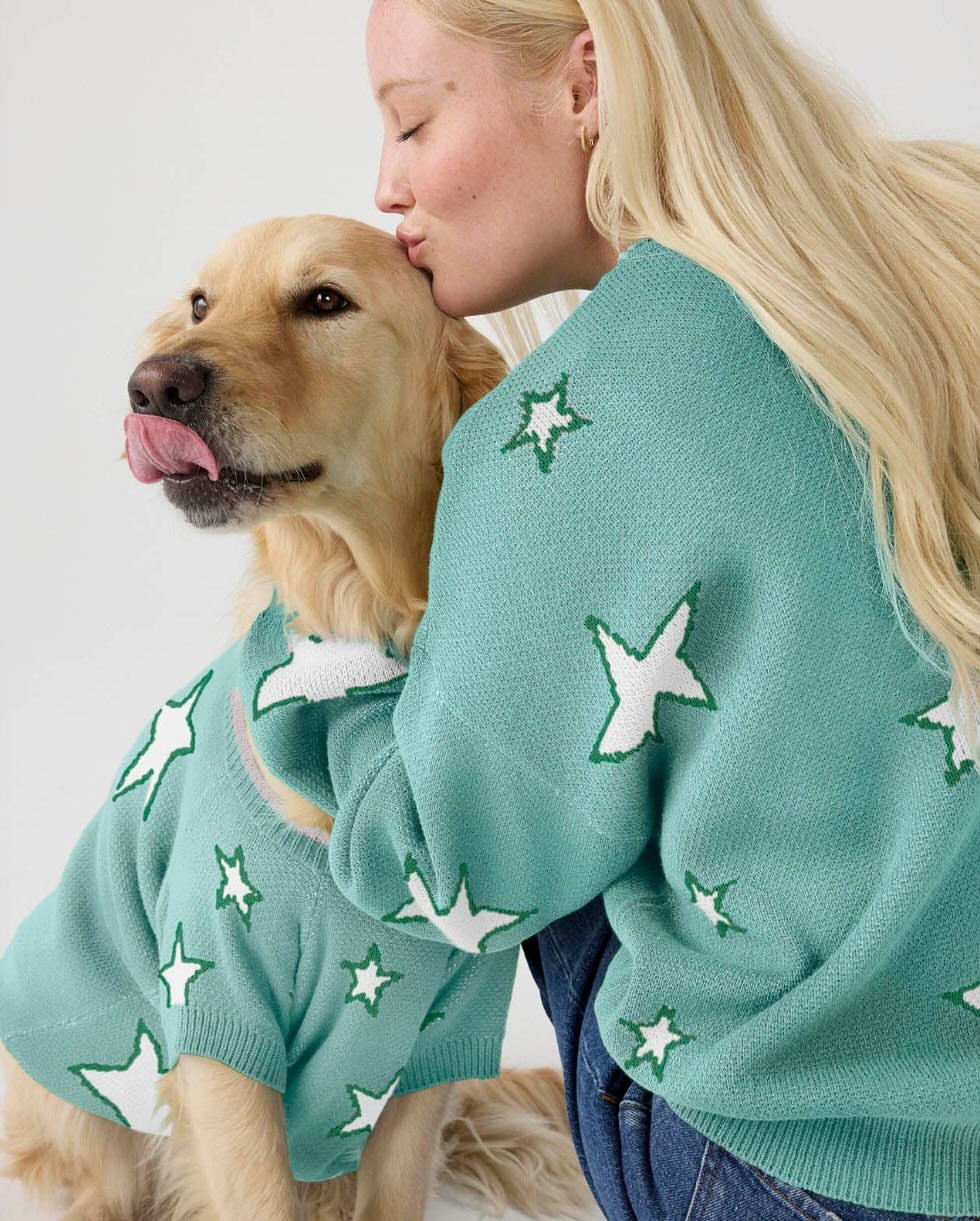 Adult female kisses Golden Retriever dog wearing matching star-patterned sweater against white background in an indoor setting.