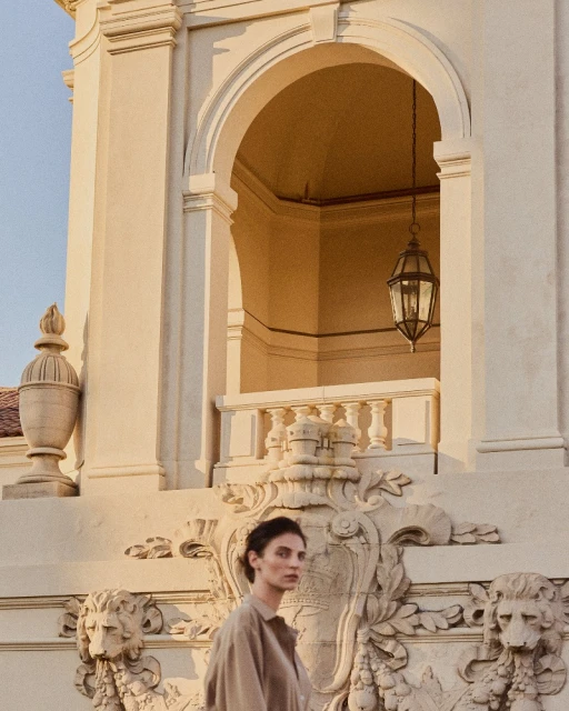 Woman in neutral shirt poses near architecture featuring columns, archways, and decorative lion sculptures under natural lighting.