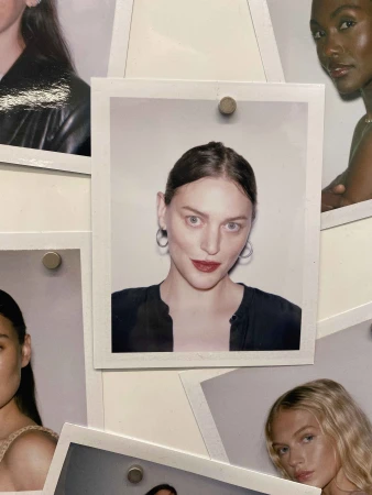 Photographs of diverse women are pinned to a wall. Polaroids showcase headshots of the women in a collage-like display.