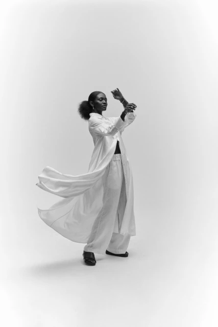 Elegant black female model in white, flowing shirt and palazzo pants strikes a dynamic pose against a stark white backdrop.