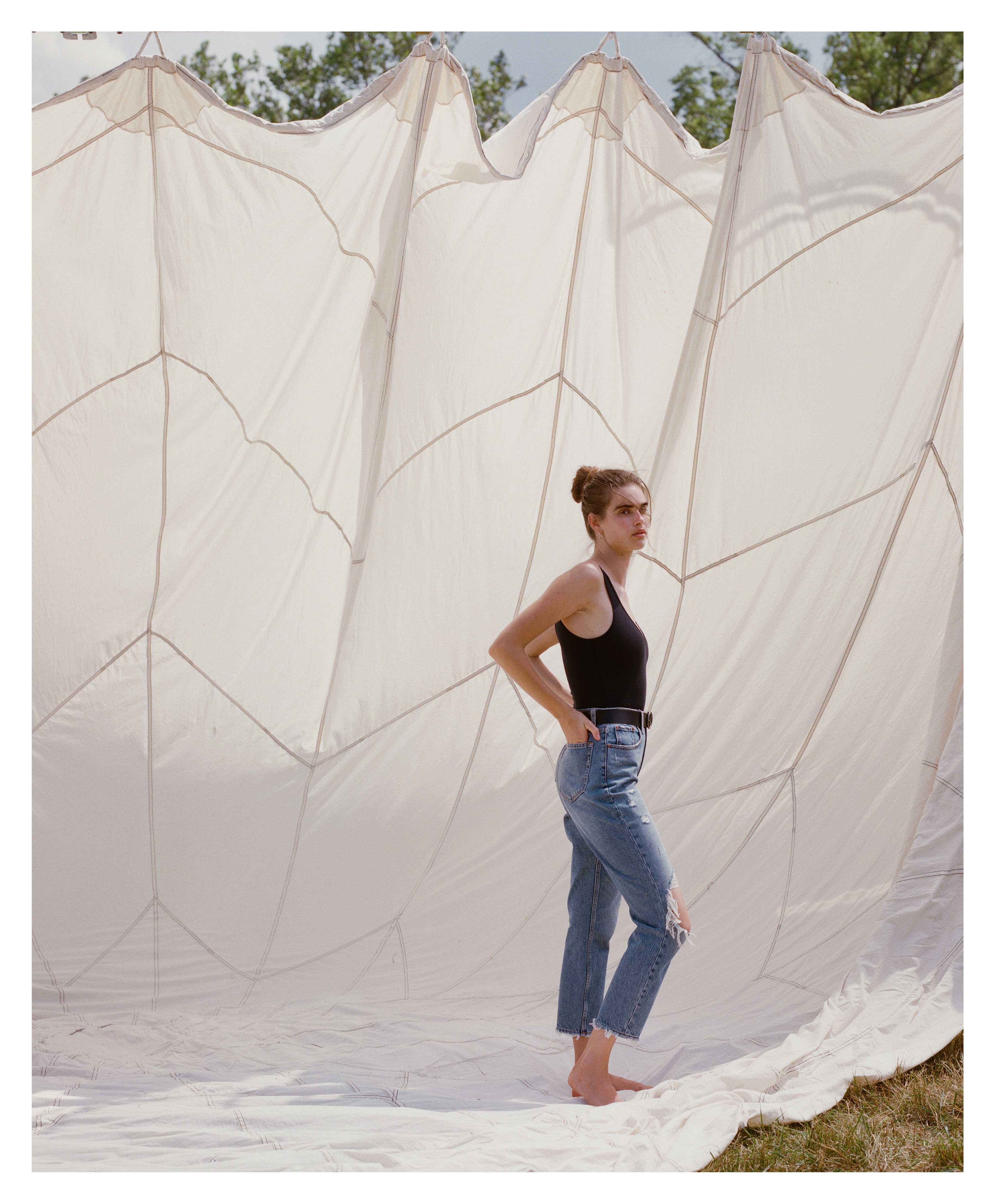 Woman in a black tank top and blue jeans standing against a large white tent backdrop outdoors