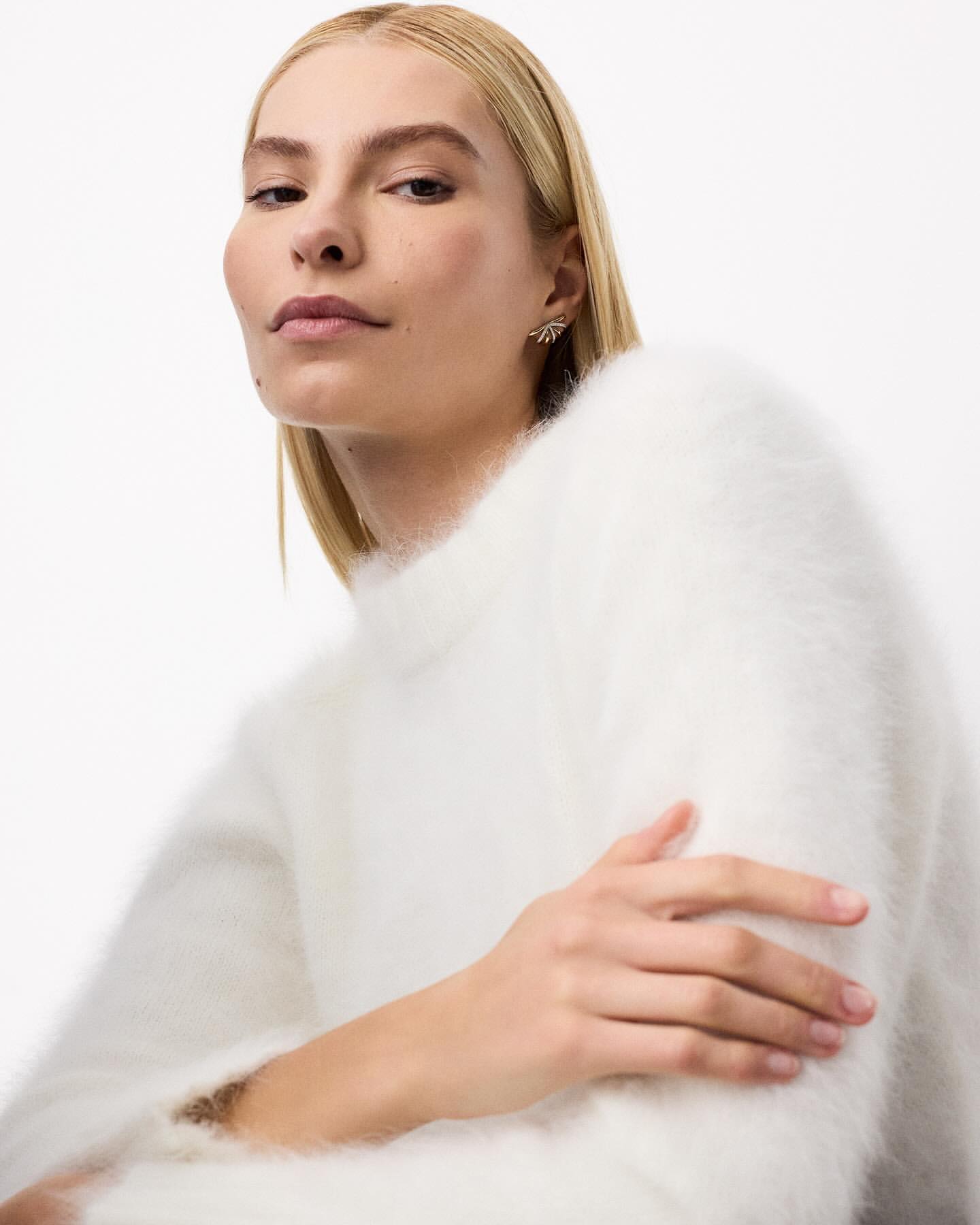 Close-up portrait of a blonde woman wearing a fluffy white sweater against a plain white background