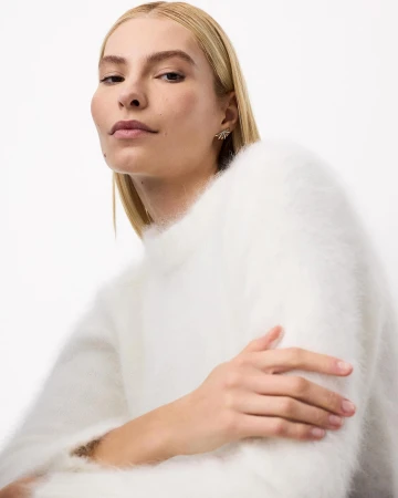 Close-up portrait of a blonde woman wearing a fluffy white sweater against a plain white background