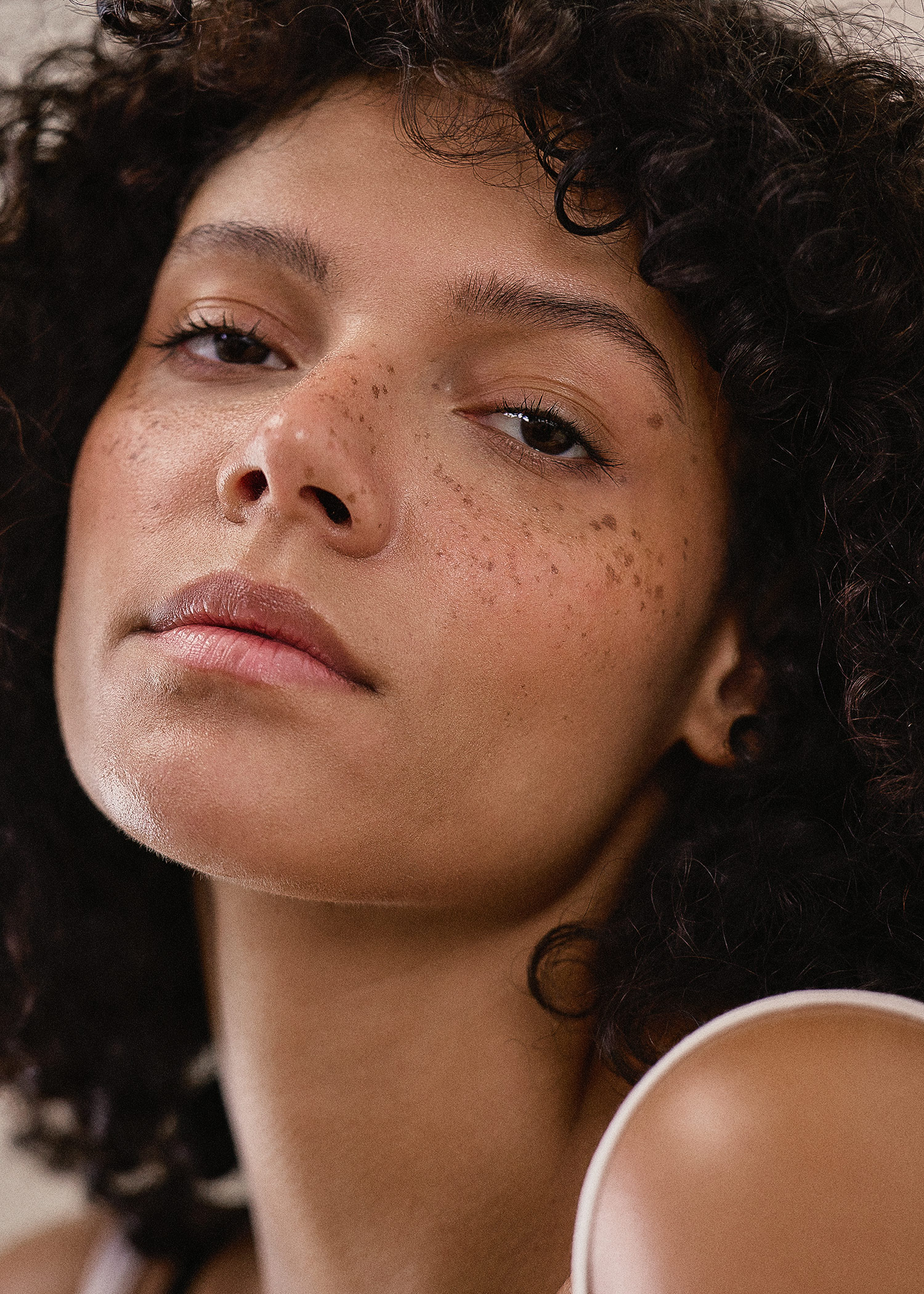 Close-up portrait of a woman with curly hair and freckles looking at the camera in a photo studio with soft, diffused lighting.