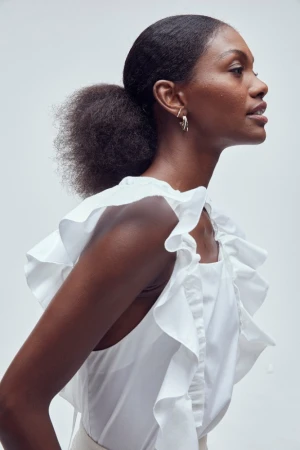 Profile portrait of a Black woman in a white ruffled top wearing hoop earrings, captured by Ari Abramczyk.