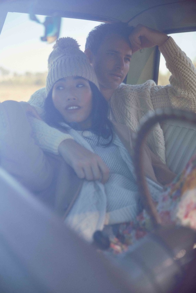 Man and woman sitting inside a vintage car, wearing knitwear and a pom-pom beanie, photographed by Annie Edmonds.