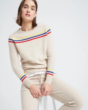 Woman seated wearing a cream cashmere sweater with colorful stripes and matching pants against a white background