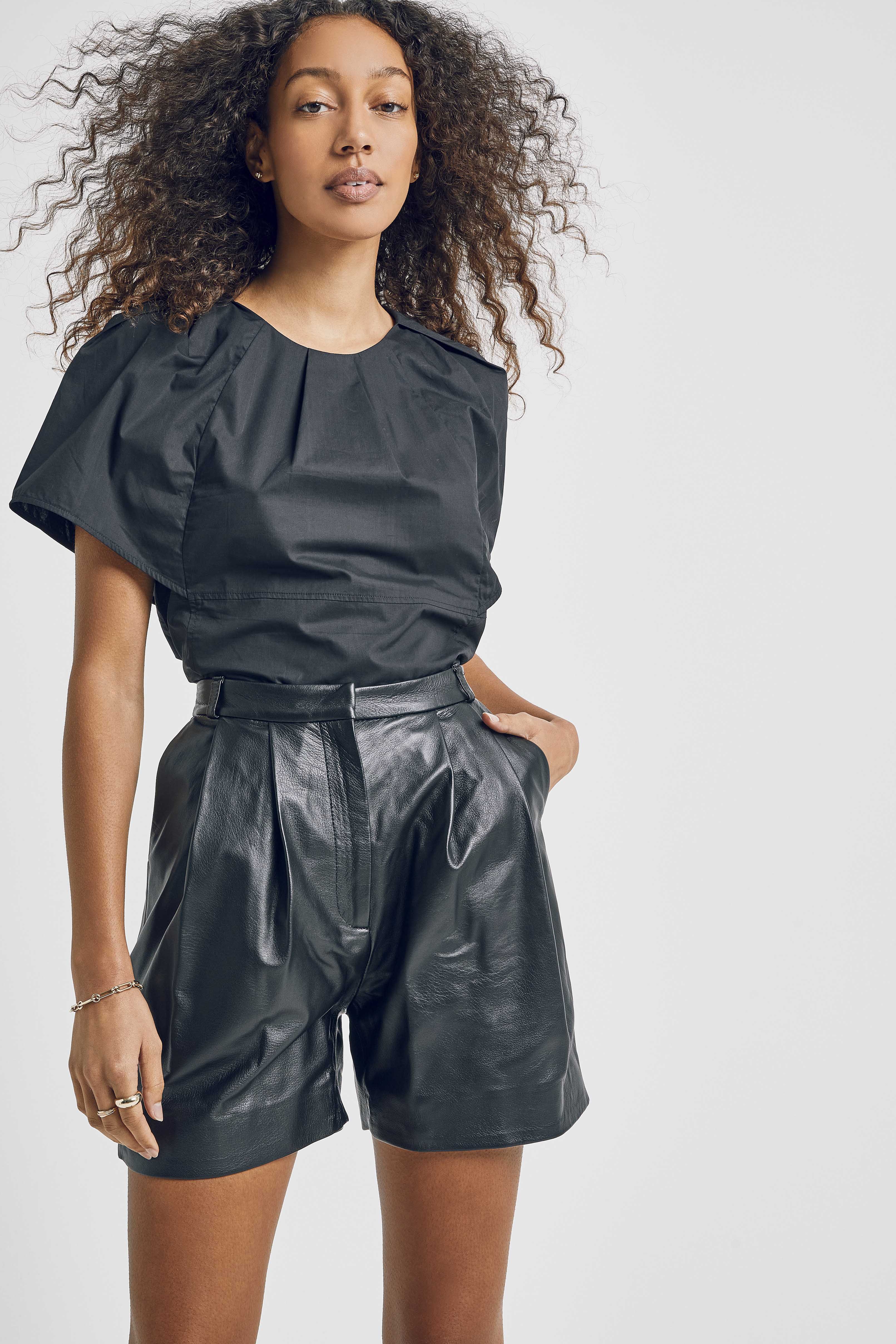 Woman in black top and shorts in a studio shot. Portrait of a female model with curly hair wearing stylish black leather shorts.