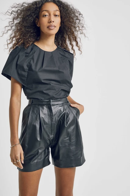 Woman in black top and shorts in a studio shot. Portrait of a female model with curly hair wearing stylish black leather shorts.