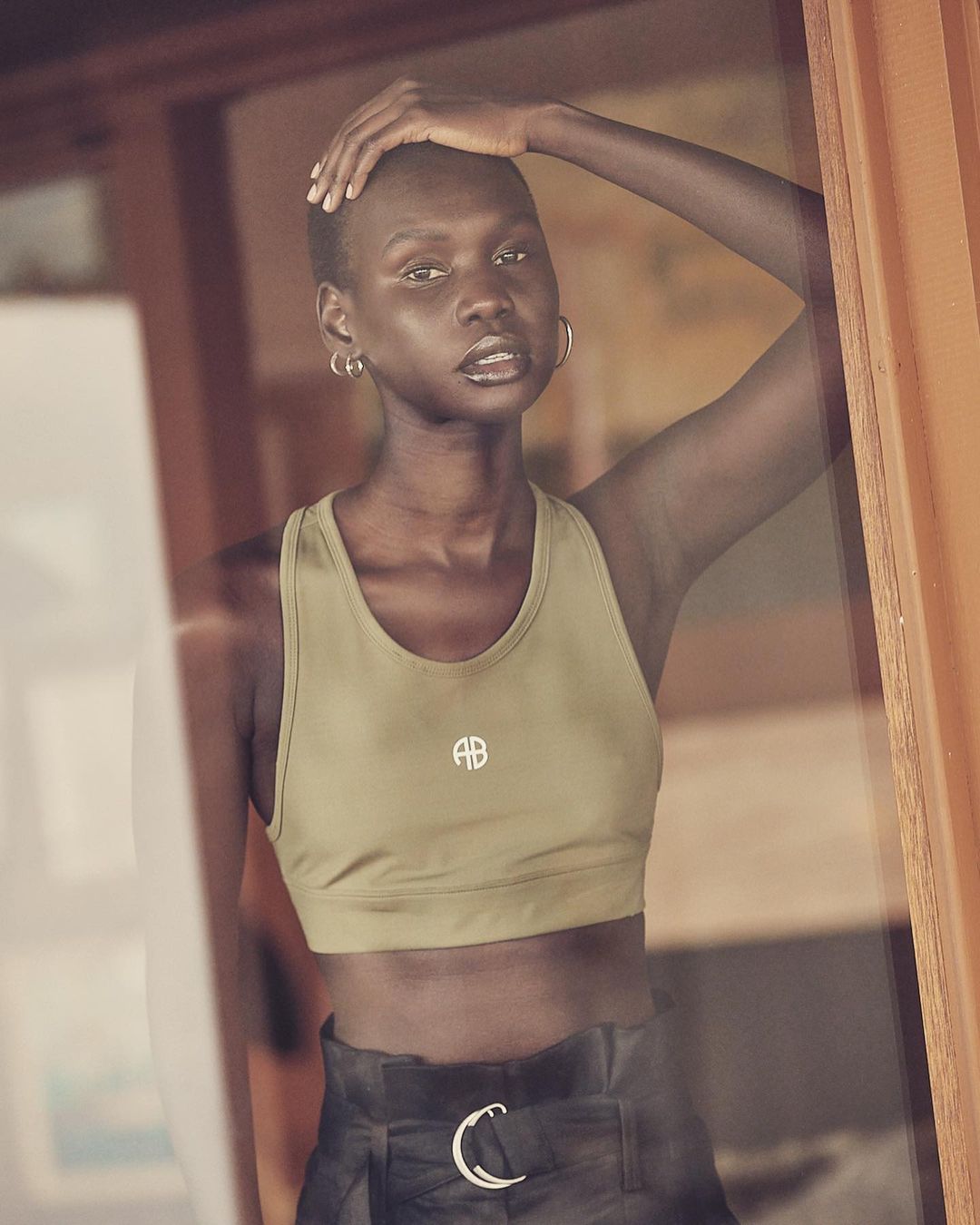 Athletic Black woman in a sports bra and high-waisted pants, looking at the camera with natural light, standing indoors.