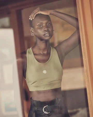 Athletic Black woman in a sports bra and high-waisted pants, looking at the camera with natural light, standing indoors.