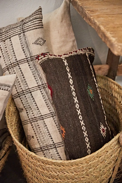 Two decorative pillows with geometric patterns are nestled in a woven straw basket, creating a cozy and textured home decor arrangement.