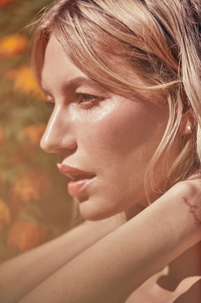 Close-up profile portrait of a blonde woman with glowing skin outdoors against a blurred floral background by Annie Edmonds