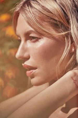 Close-up profile portrait of a blonde woman with glowing skin outdoors against a blurred floral background by Annie Edmonds