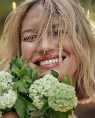 Close-up portrait of a smiling blonde woman holding pale green hydrangeas in Los Angeles shot by Annie Edmonds.