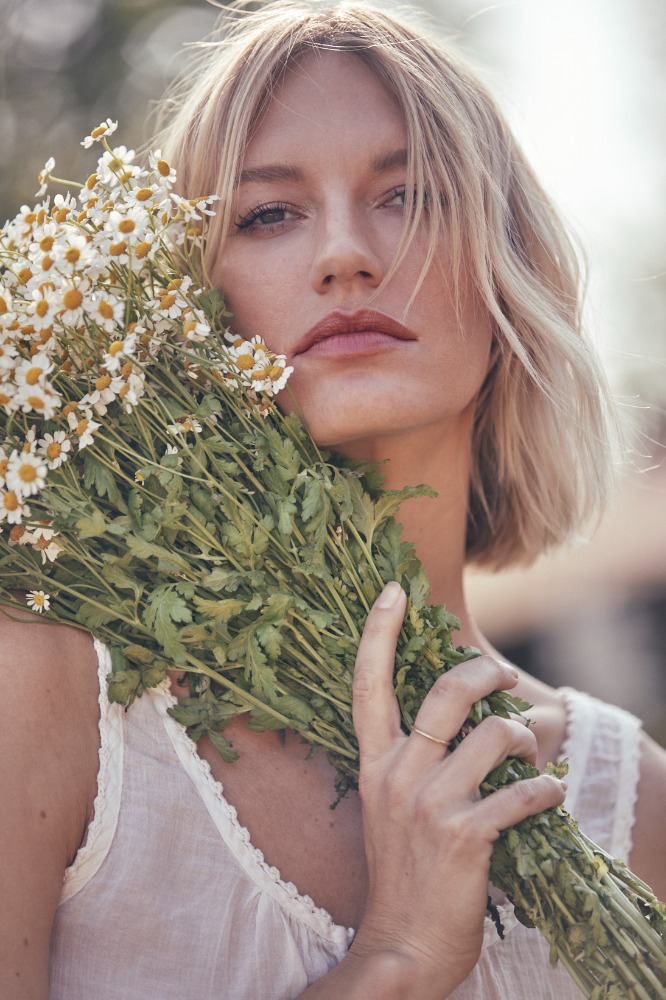 Close-up portrait of a blonde woman holding a large bunch of white wildflowers against an out-of-focus background.