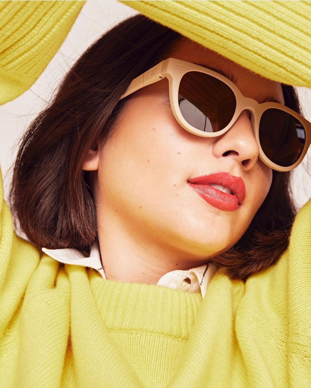 Woman wearing sunglasses and a yellow sweater. Close-up portrait of a fashionable model with dark hair and coral lipstick.