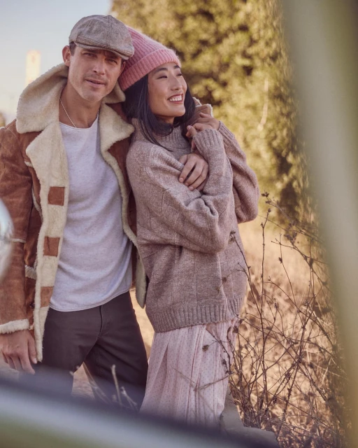 Couple posing outdoors in autumn: A man in a cap and jacket with a woman wearing a pink beanie and sweater.