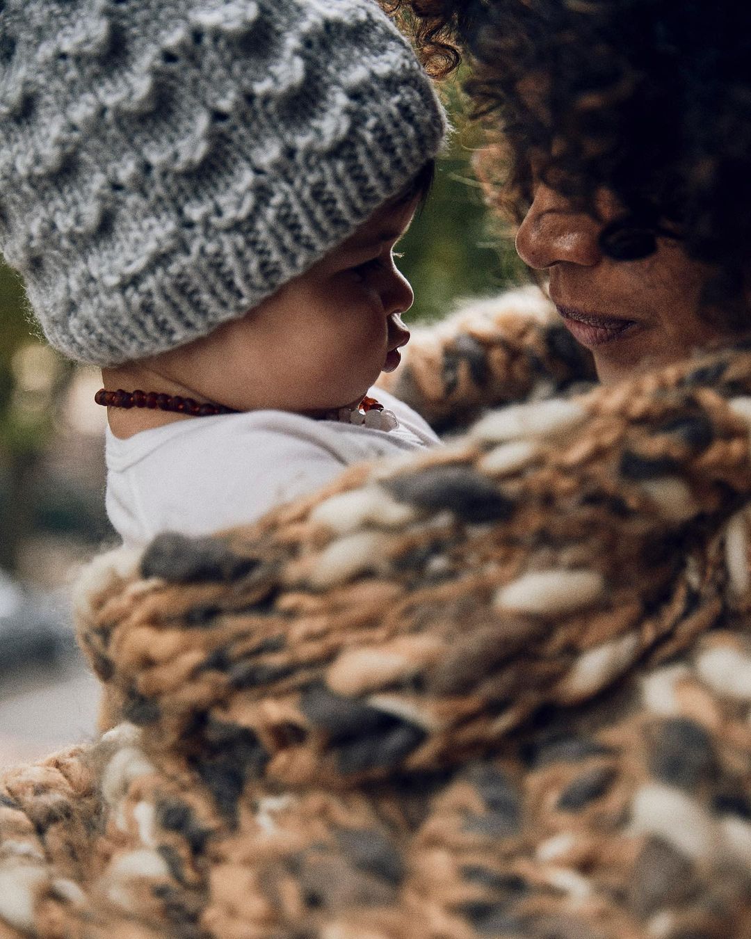 Close-up portrait of an adult holding an infant wearing a grey knit beanie and white bodysuit, photographed by Annie Edmonds.