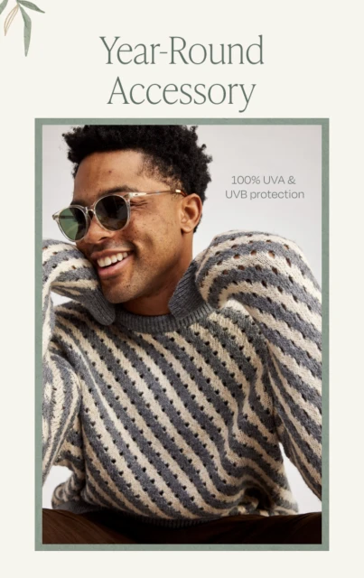 A smiling black male model wears sunglasses and a patterned sweater, showcasing fashion and eye protection.