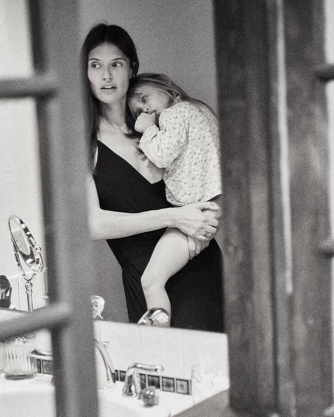 Black and white portrait of a woman holding a young child in a domestic bathroom captured by Annie Edmonds.
