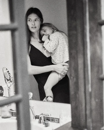 Black and white portrait of a woman holding a young child in a domestic bathroom captured by Annie Edmonds.