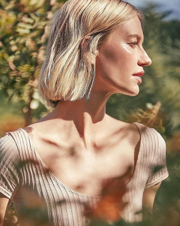 Close-up profile portrait of a blonde woman wearing a ribbed beige top outdoors in natural sunlight with dappled shadows
