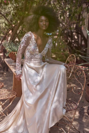 Black woman with voluminous afro hair wearing an off-white silk and lace gown seated on an ornate metal chair outdoors.