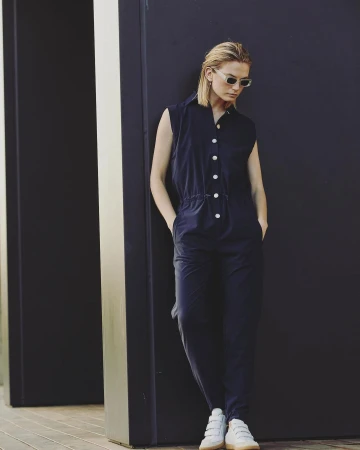 Woman in dark jumpsuit and sunglasses leaning against a dark wall photographed by Annie Edmonds