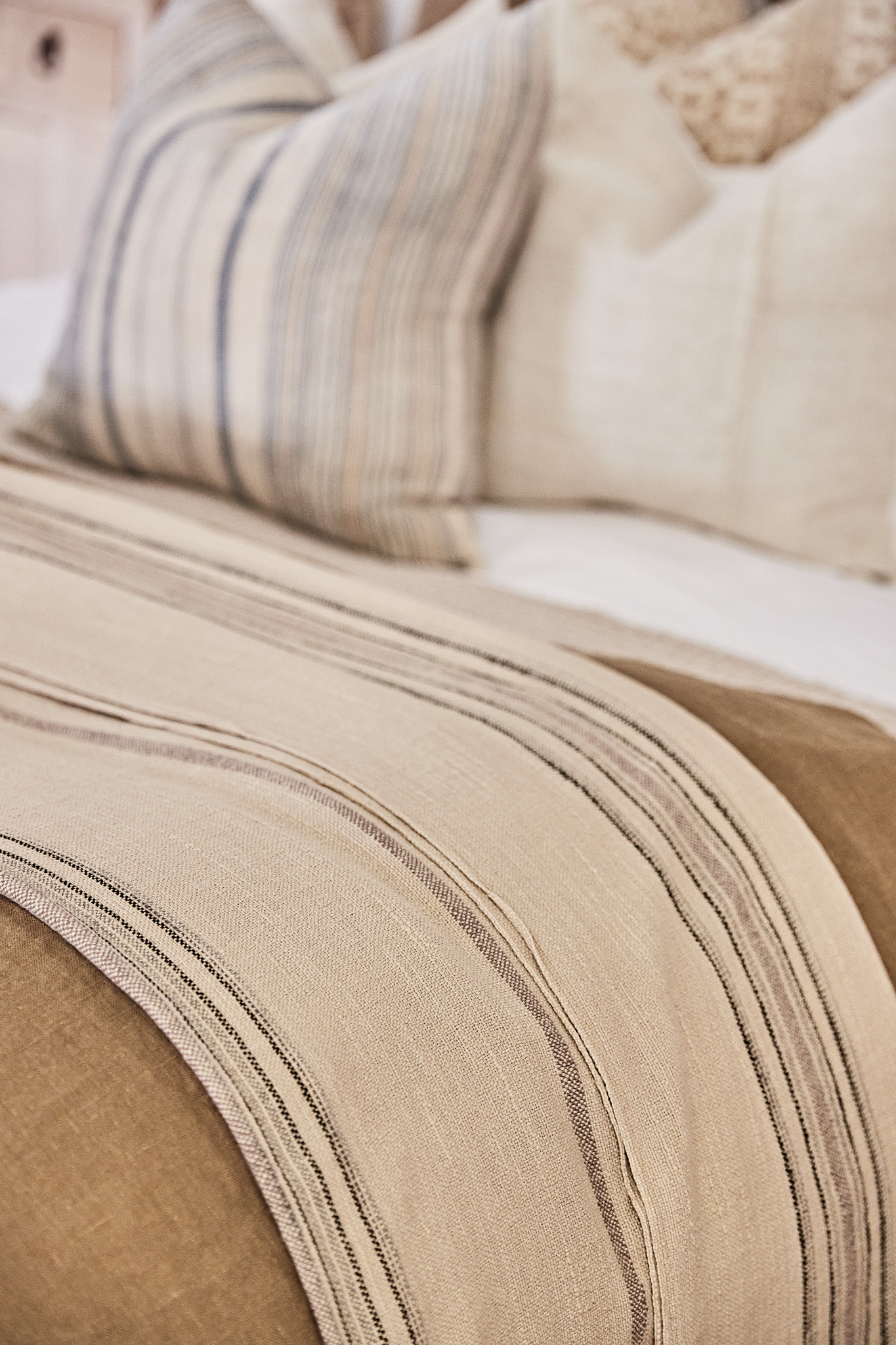 Close-up on a made bed featuring a striped throw blanket and patterned pillows, showcasing a cozy and inviting interior design aesthetic.