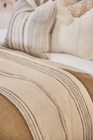 Close-up on a made bed featuring a striped throw blanket and patterned pillows, showcasing a cozy and inviting interior design aesthetic.
