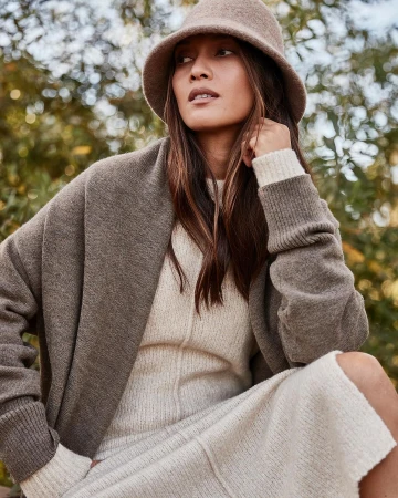 Woman wearing a felt bucket hat and knit cardigan over a cream dress outdoors