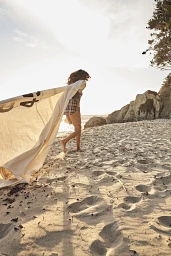 Woman running on a sandy beach holding a large piece of fabric caught in the wind, photographed by Annie Edmonds.
