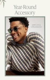 Man wearing sunglasses and a grey and white striped sweater smiling against a white seamless background
