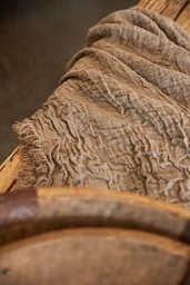 Close-up of textured beige linen textile draped over a rustic wooden surface photographed by Annie Edmonds