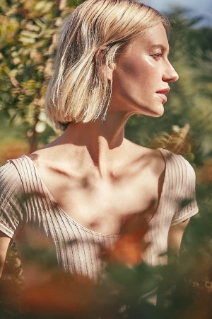 Portrait of a blonde woman wearing a ribbed top and long earrings outdoors in soft natural light.