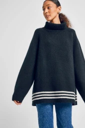 Woman wearing an oversized dark turtleneck sweater with white stripes and blue jeans against a white background