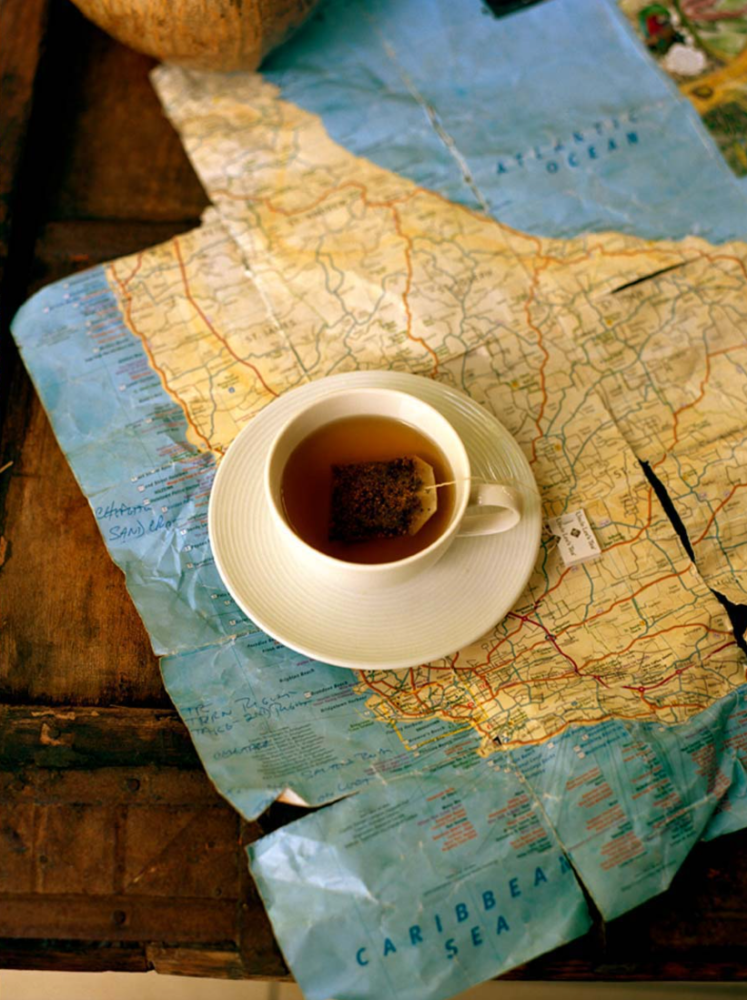 Overhead shot of a white teacup filled with tea on a saucer, set on a vintage world map on a rustic wood surface.