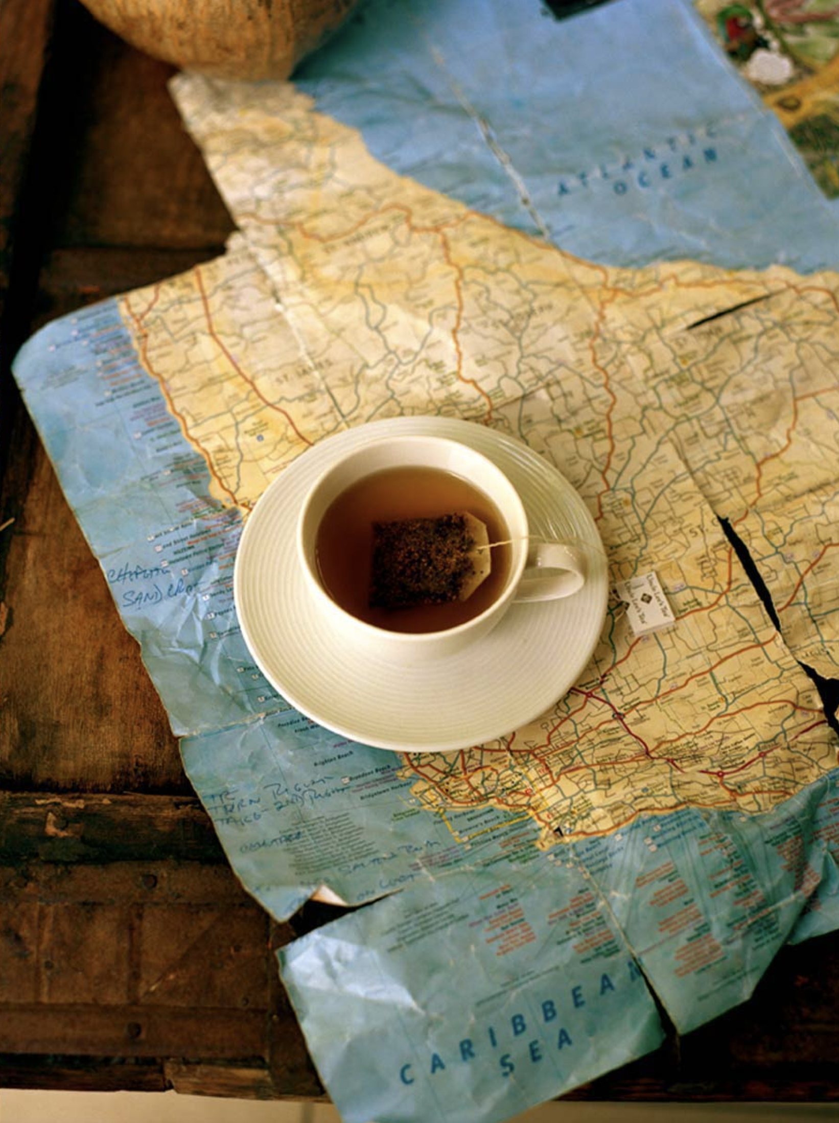 A cup of tea rests on a map of the Caribbean Sea, with a vintage coconut shell on a rustic wooden surface. Still life.