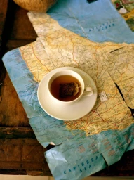 A white teacup with a tea bag resting on a saucer atop a crumpled vintage world map on a wooden surface.