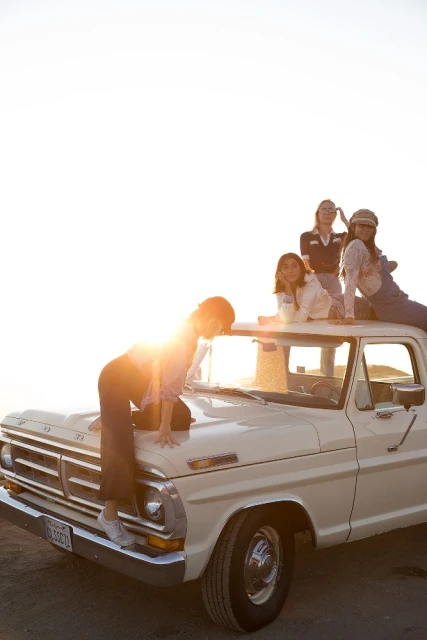 Group of girls on the hood and roof of a vintage Ford pickup truck, bathed in warm sunlight, evoking a sense of youthful freedom and friendship.