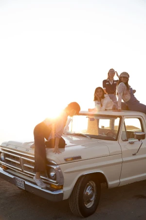 Group of girls on the hood and roof of a vintage Ford pickup truck, bathed in warm sunlight, evoking a sense of youthful freedom and friendship.