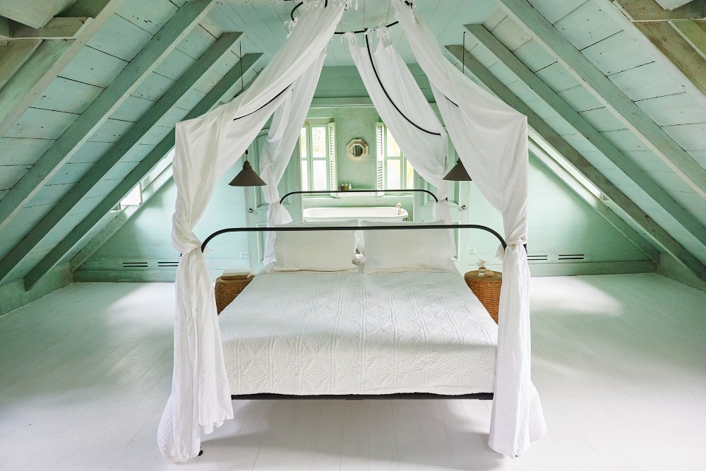 Bedroom interior featuring a canopy bed with white linens, light green painted walls and ceiling, and natural light from windows.