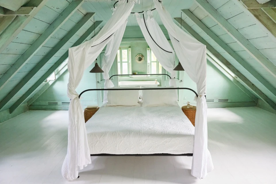 Bedroom interior featuring a canopy bed with white linens, light green painted walls and ceiling, and natural light from windows.