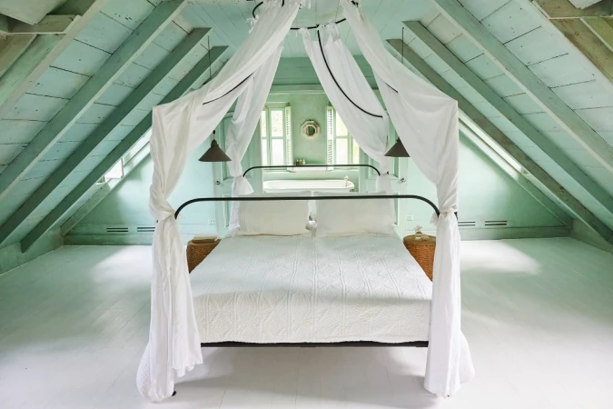 Bedroom interior featuring a canopy bed with white linens, light green painted walls and ceiling, and natural light from windows.