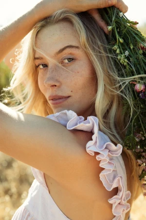Close-up portrait of a woman with blonde hair and freckles holding a bouquet of wildflowers by photographer Cheyenne Ellis.