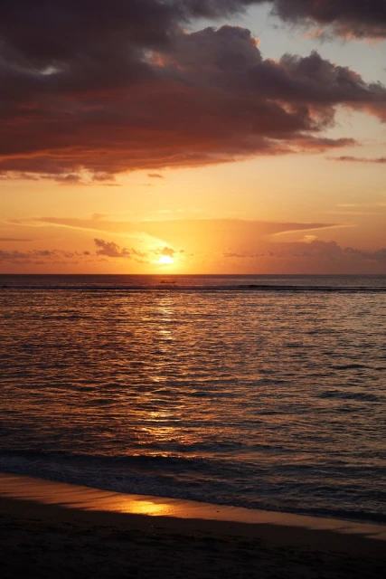 Golden sunset over a calm ocean with dark clouds above reflecting in the water and sand on the beach in vertical landscape format.