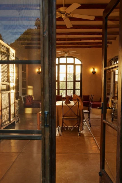 Interior view through doorway of a dining room with table and chairs, sofa, and arched window, with warm lighting and neutral palette.