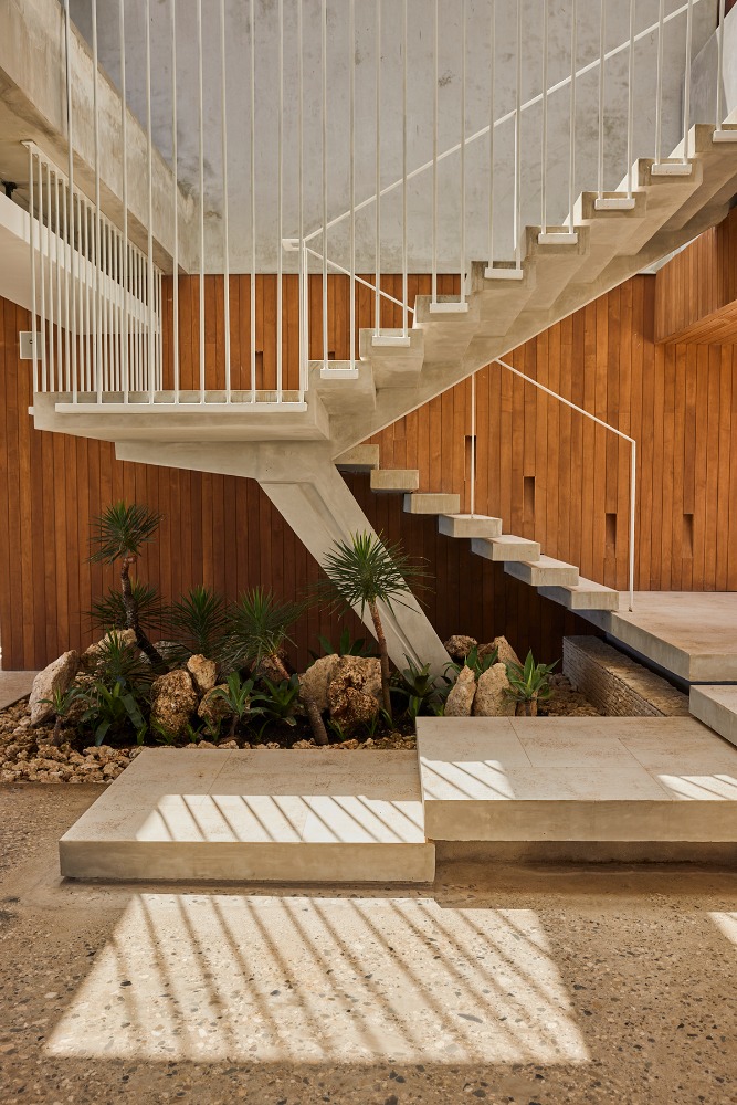 Concrete staircase with white railing and plants beneath in a modern home with wood paneling and patterned floor shadows.