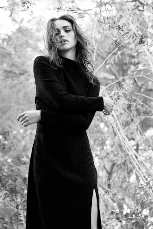 Black and white portrait of a woman in a long-sleeved knitted dress outdoors amongst foliage, photographed by Cheyenne Ellis.